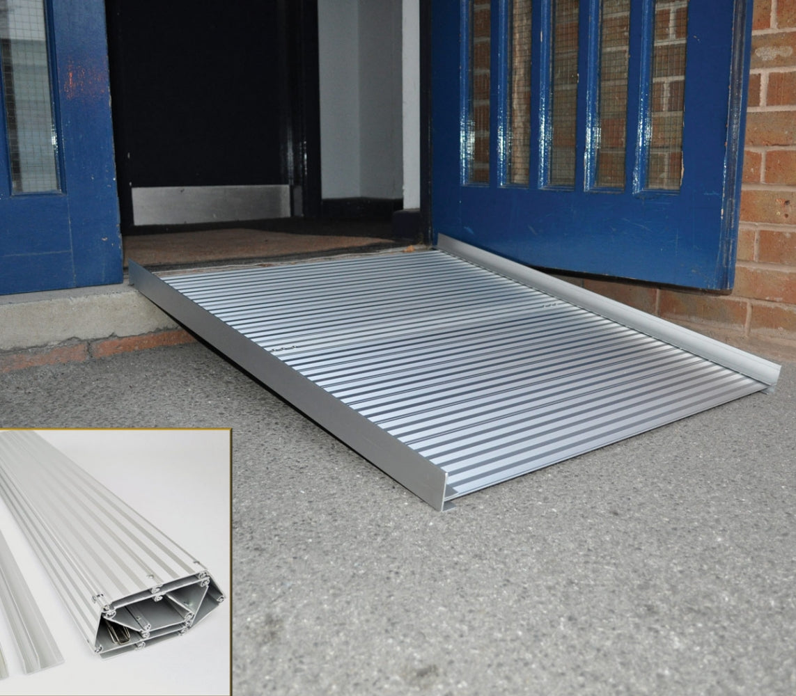 Rampa enrollable de aluminio para silla de ruedas de Able2 Shop, colocada frente a la puerta azul, con superficie acanalada antideslizante.